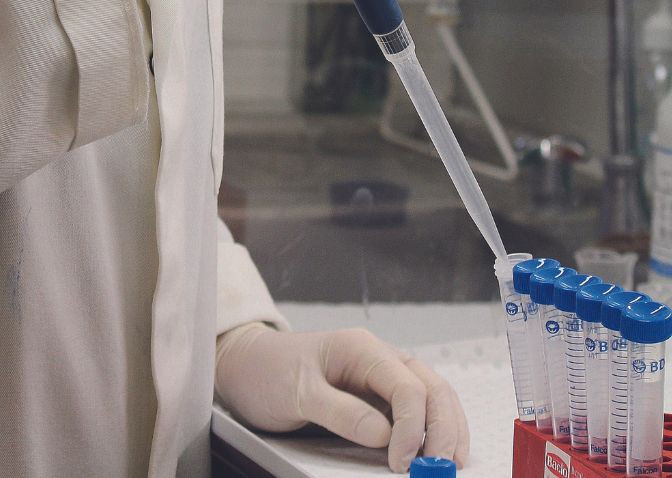 person in lab coat pulling samples from test tubes
